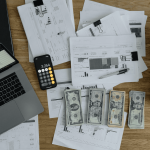 dollars on a desk with a laptop, documents and a calculator