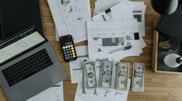 dollars on a desk with a laptop, documents and a calculator